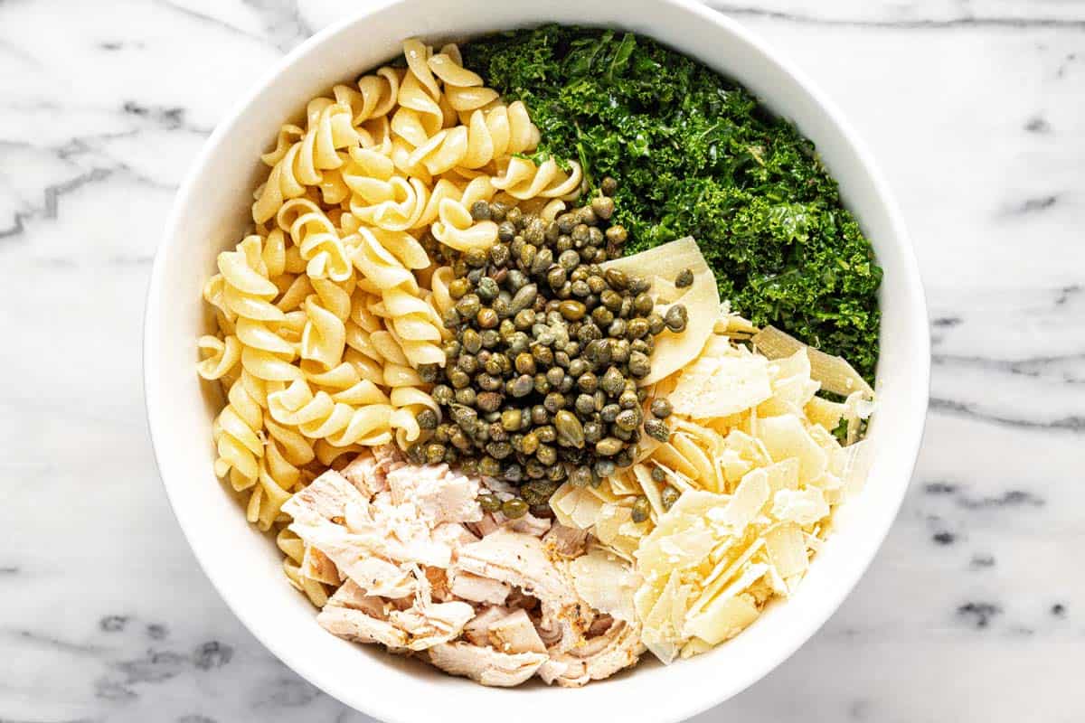 Large bowl filled with ingredients to make chicken Caesar pasta salad. 