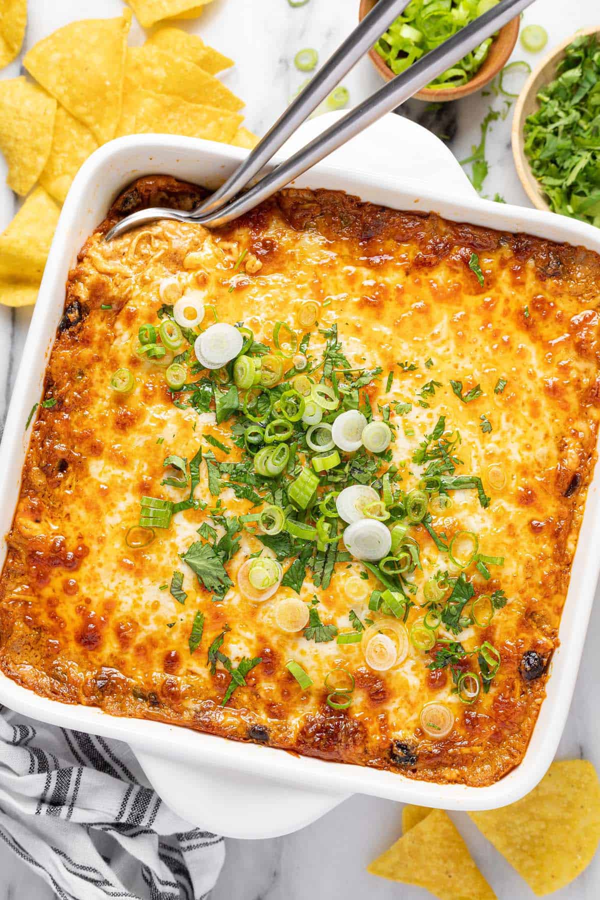 Square baking dish filled with homemade cheesy chicken enchilada dip garnished with cilantro and green onion. 