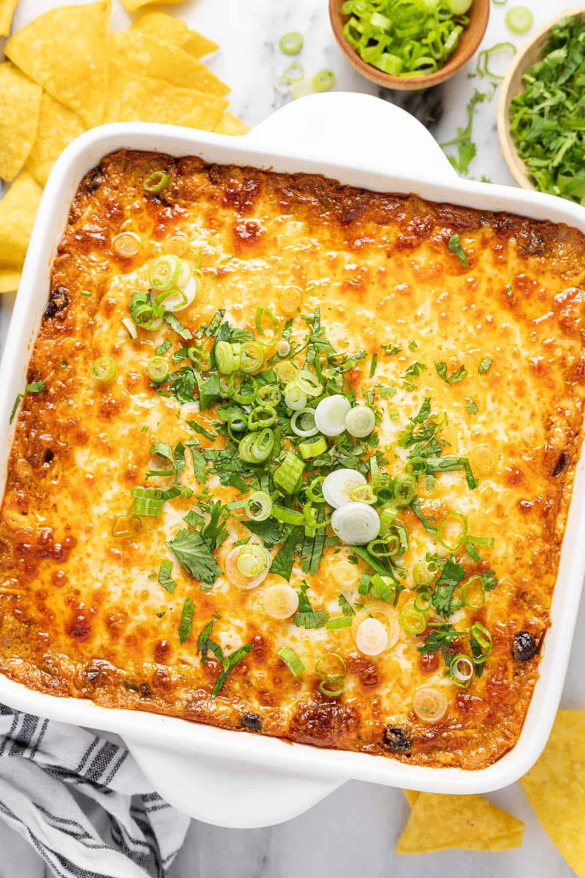 Square baking dish filled with homemade cheesy chicken enchilada dip garnished with cilantro and green onion. 