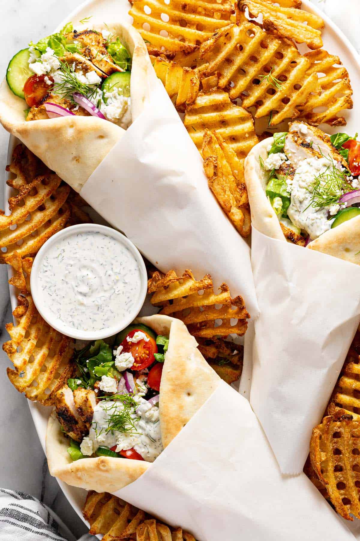 Large platter filled with Greek chicken gyros and waffle fries. 