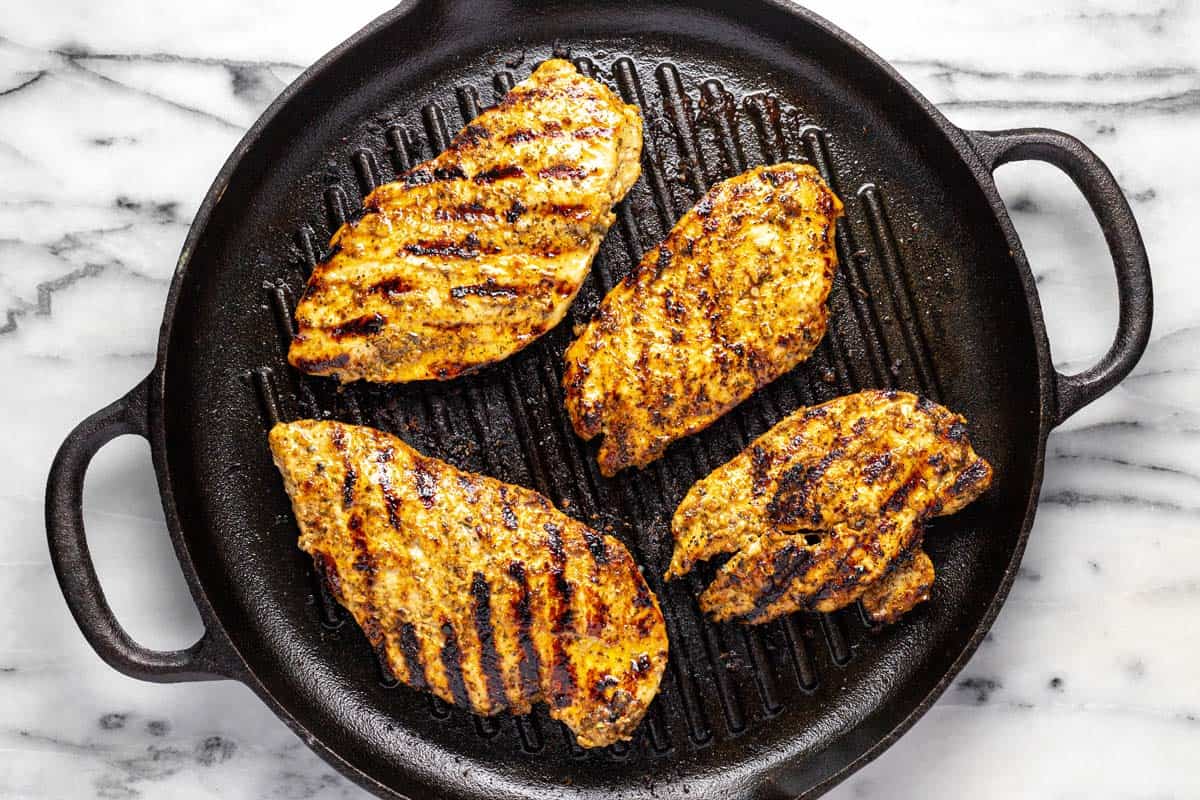 Large cast iron pan with grilled Greek chicken breasts. 