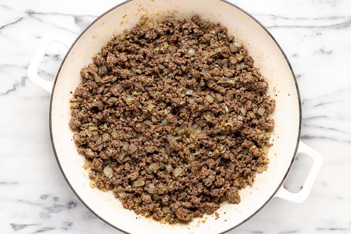 Large sauté pan filled with browned ground beef and diced onion. 