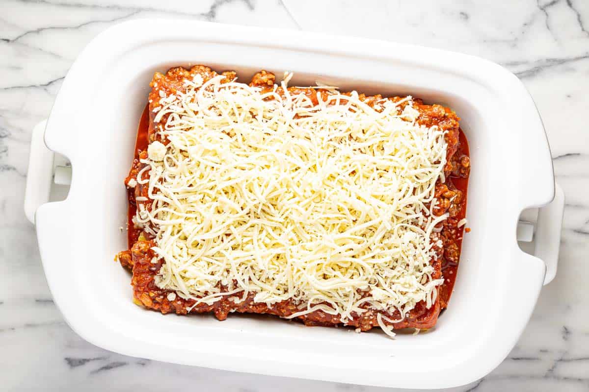 Slow cooker lasagna topped with cheese ready to be cooked. 