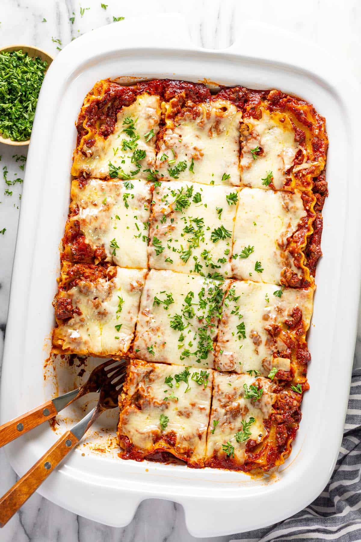 Crock pot lasagna sliced into squares garnished with fresh chopped parsley. 