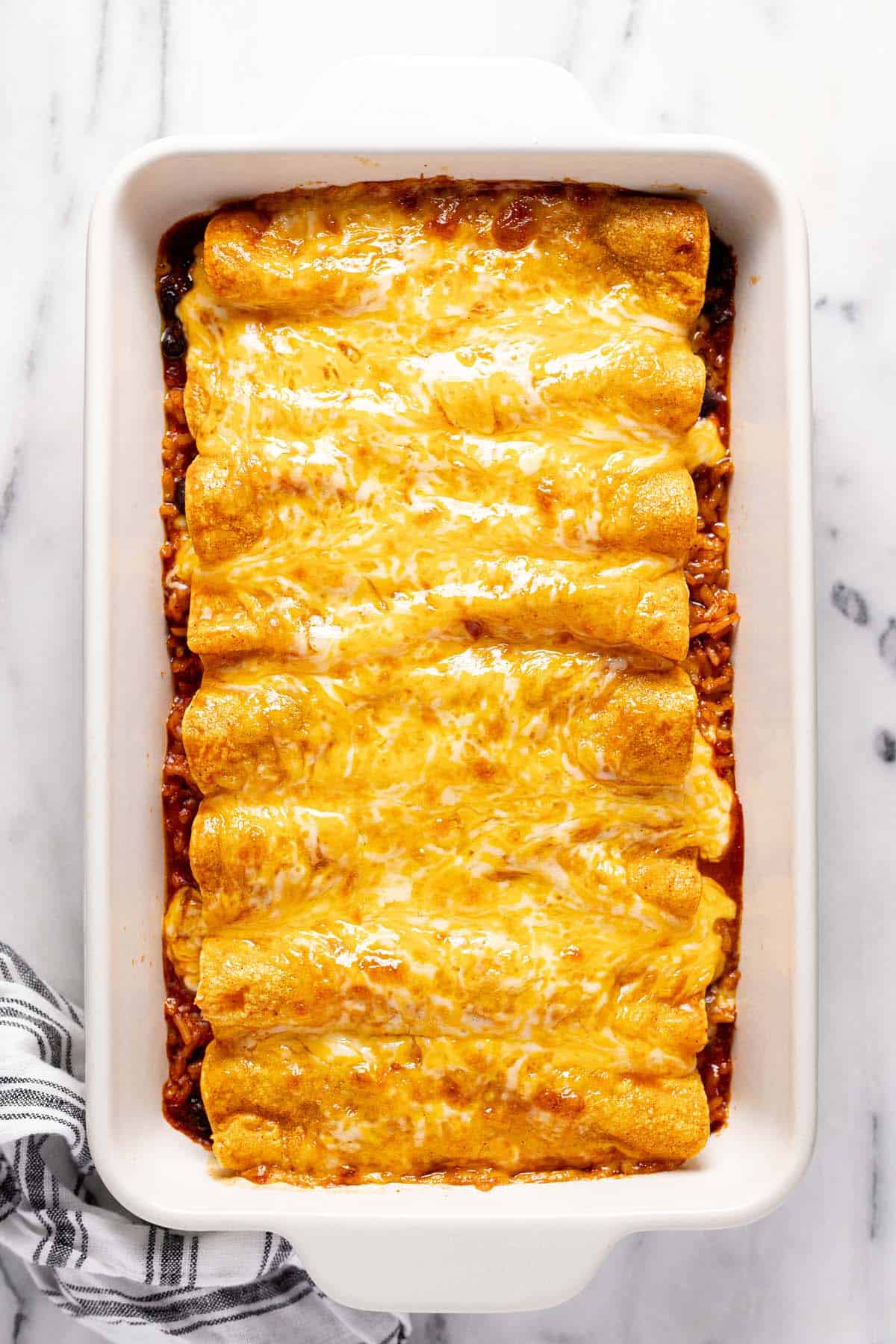 Ground beef enchiladas topped with melted cheese on a bed of rice. 