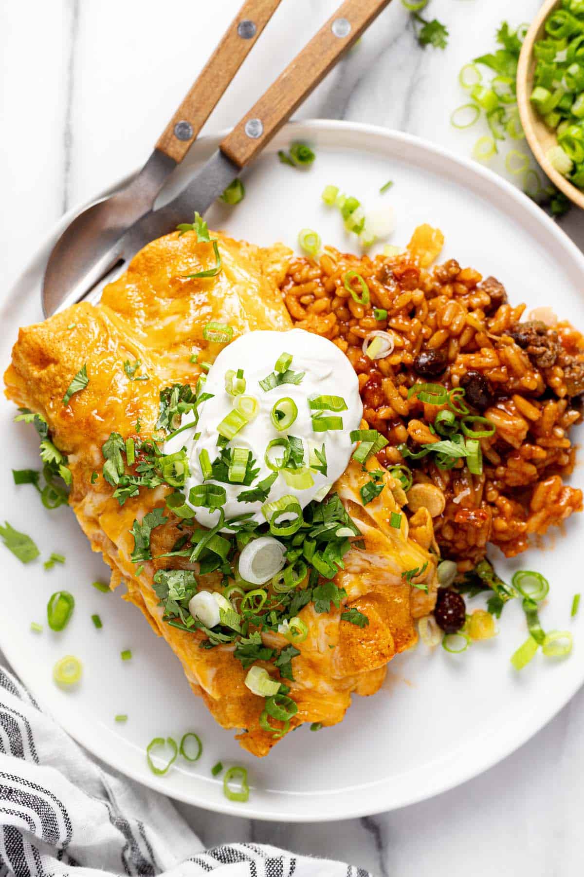 Enchiladas and rice topped with sour cream on a plate. 