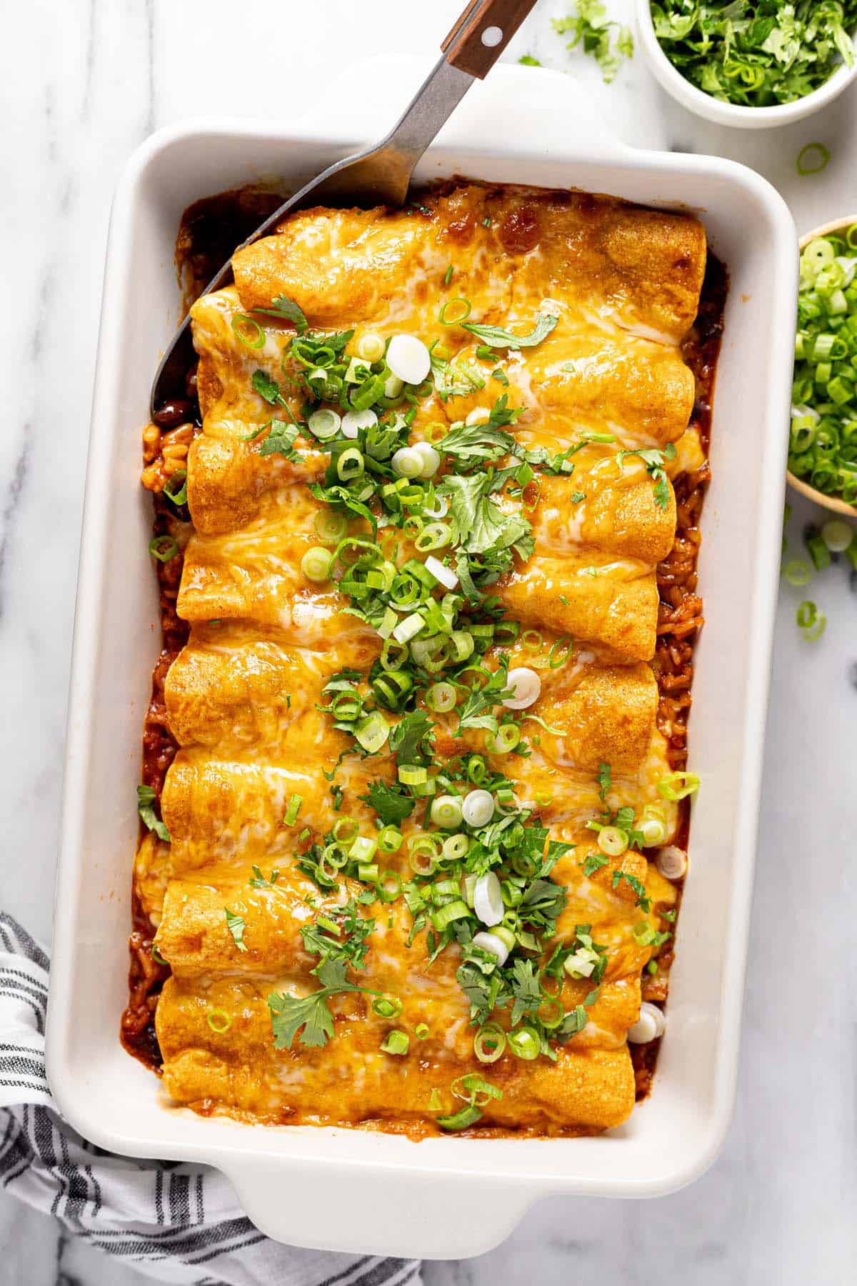 Large pan of enchiladas topped with green onions and cilantro. 