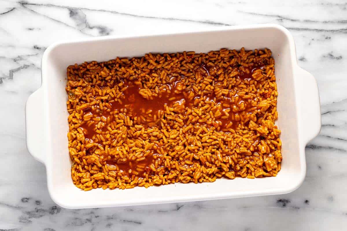 Baking dish with Spanish rice and enchilada sauce in it. 