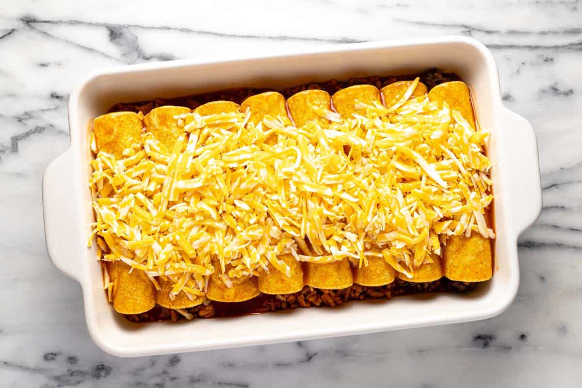 Homemade ground beef enchiladas topped with cheese in a large baking dish. 