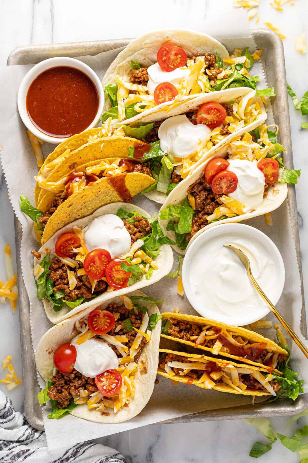 Metal tray with crispy and soft tacos with taco sauce and sour cream. 