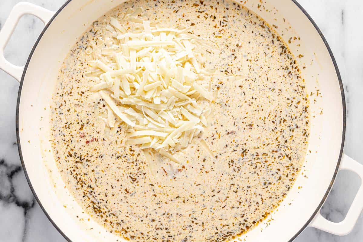 Large pan with cream sauce and shredded Parmesan being added. 