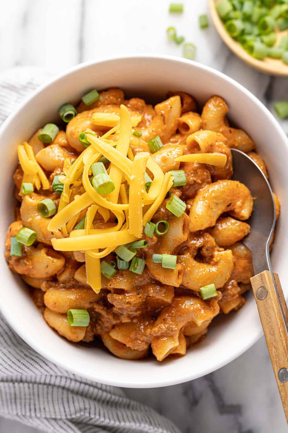 Small bowl filled with homemade beefaroni topped with cheese and green onions. 