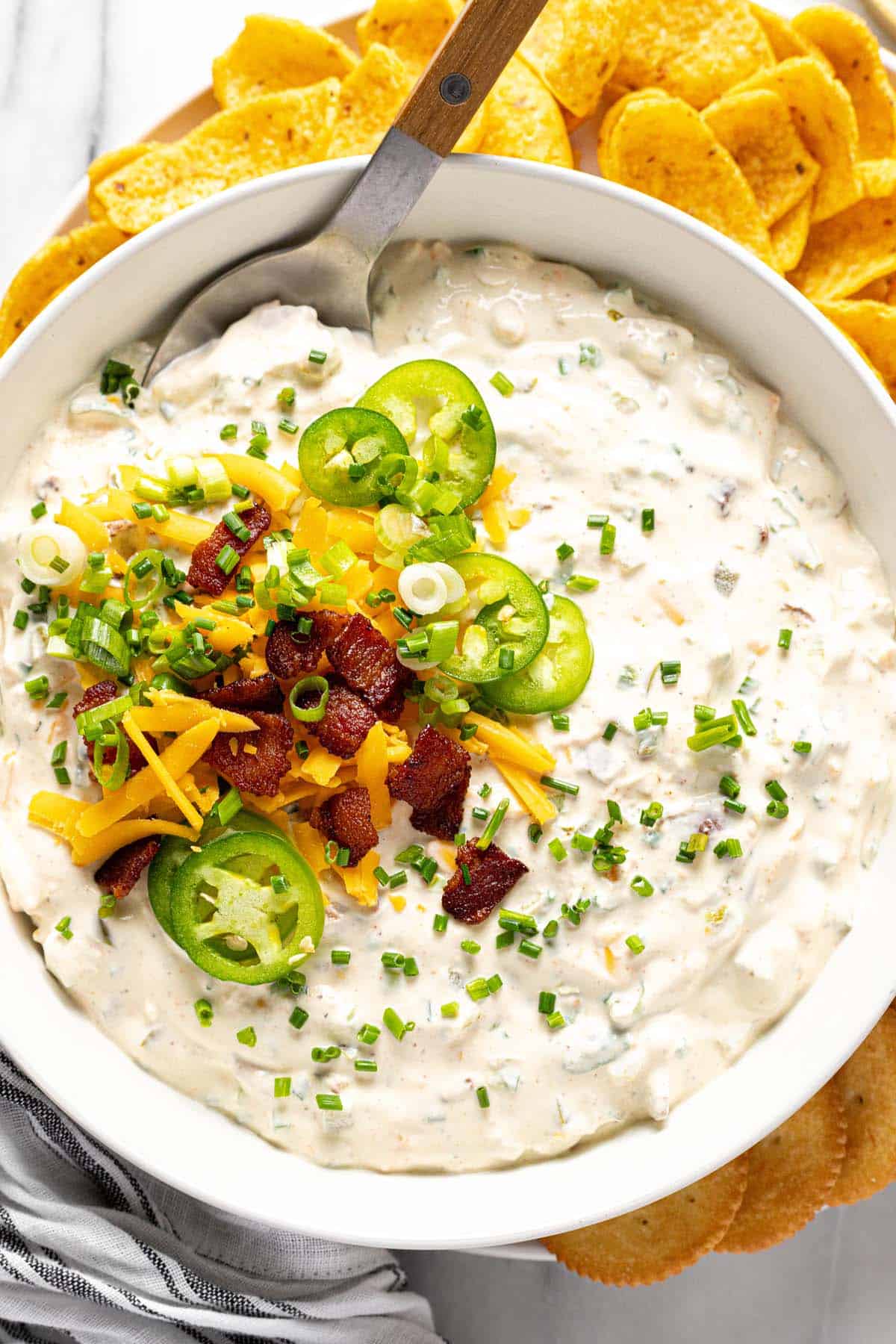 Bowl of cold jalapeno dip garnished with cheese, bacon, and sliced jalapenos. 