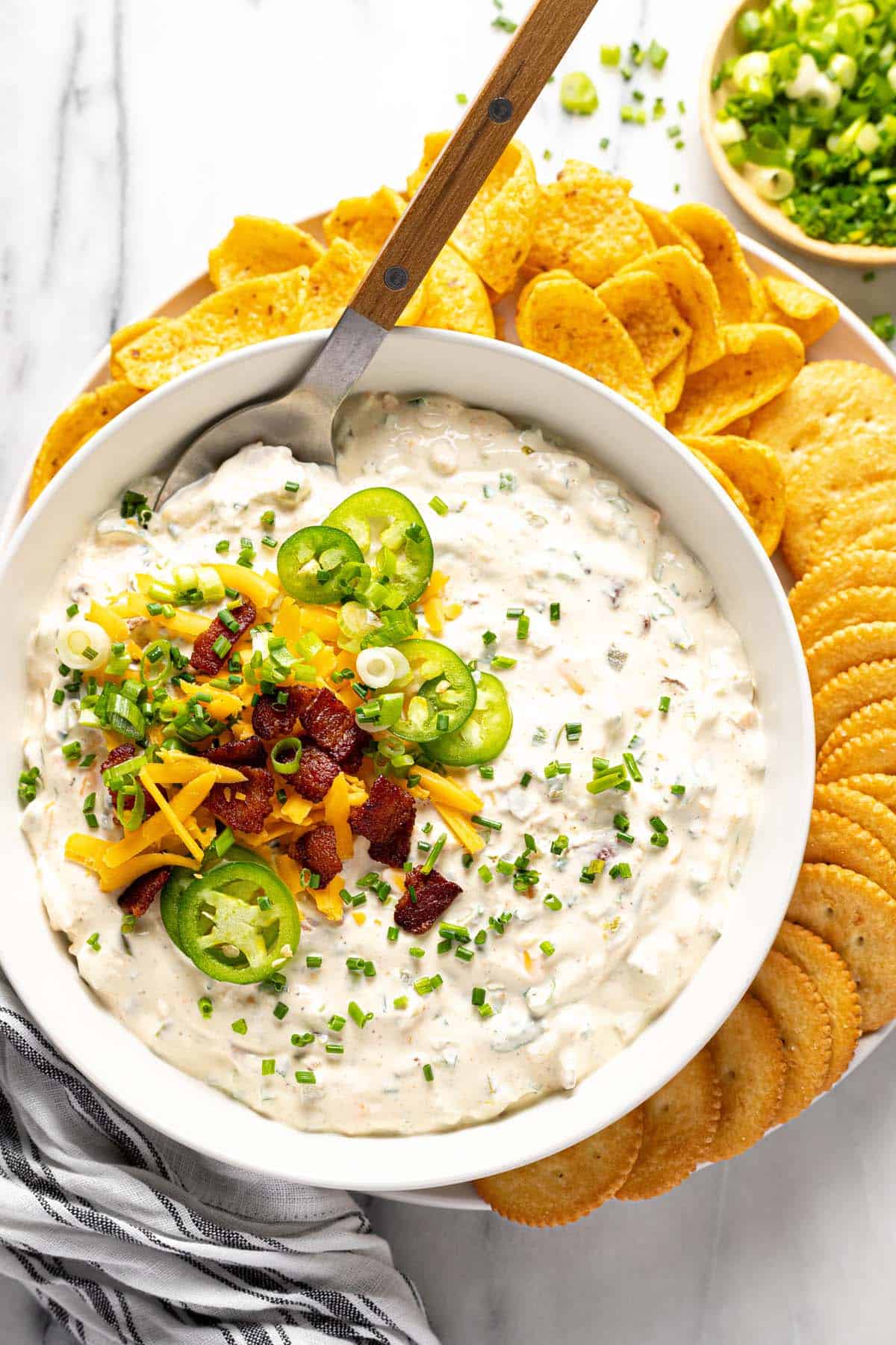 Bowl of cold jalapeno dip garnished with cheese, bacon, and sliced jalapenos. 