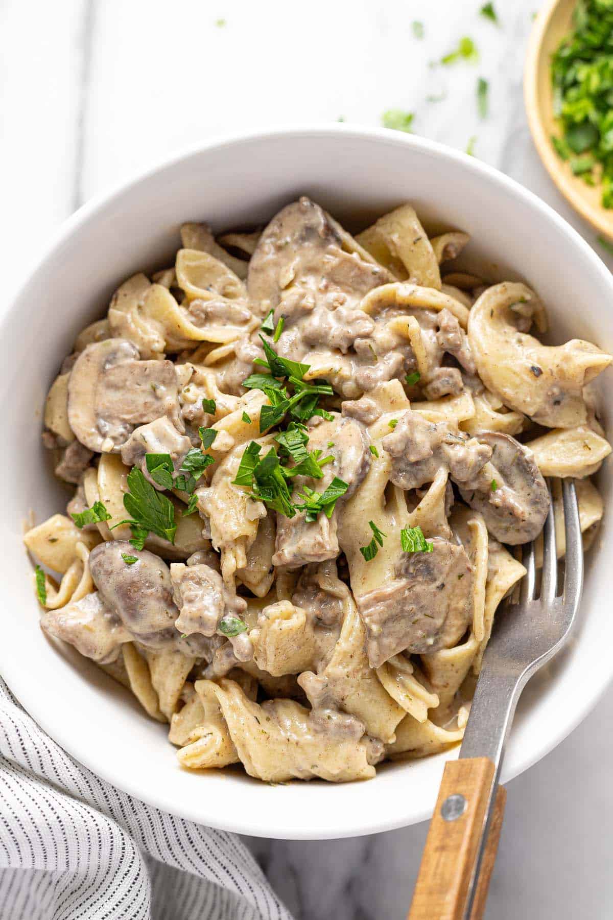 Bowl of ground beef stroganoff and egg noodles garnished with parsley. 