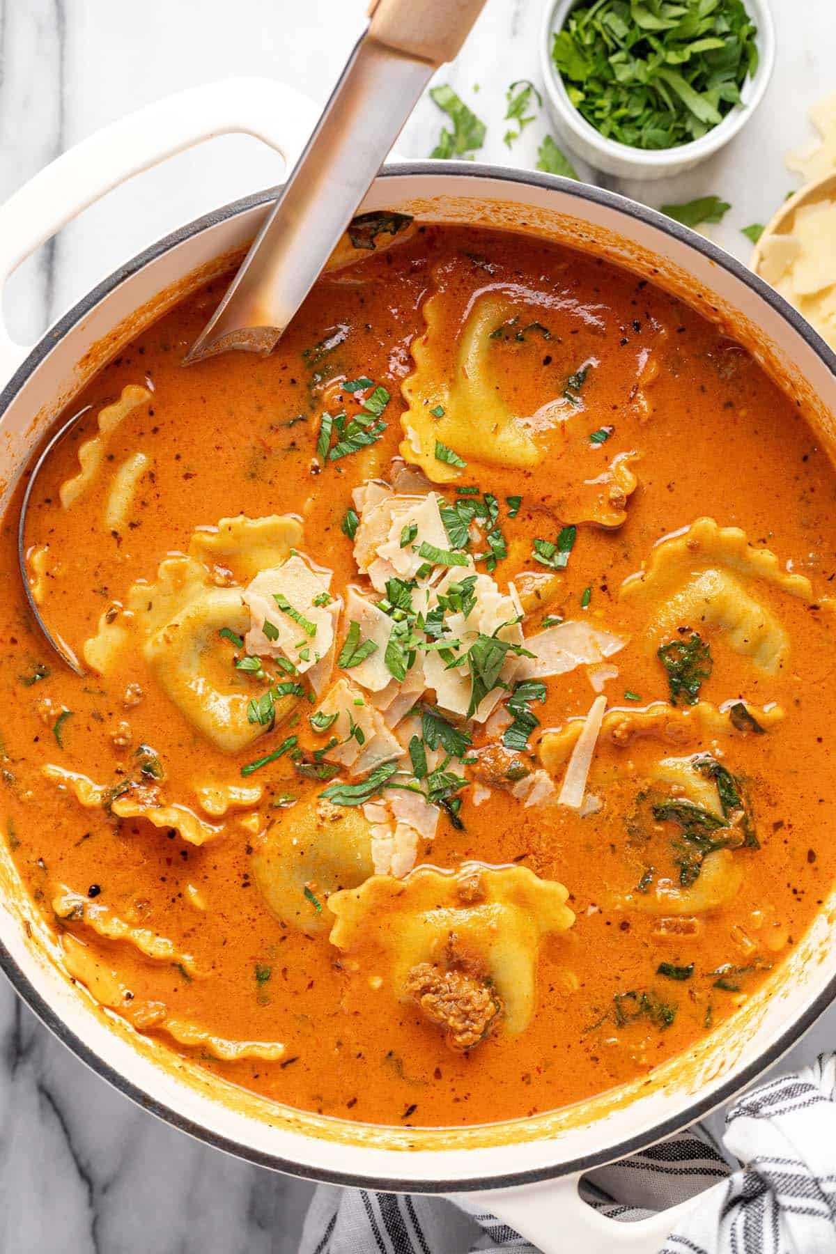 Large pot of creamy ravioli soup garnished with Parmesan and parsley. 