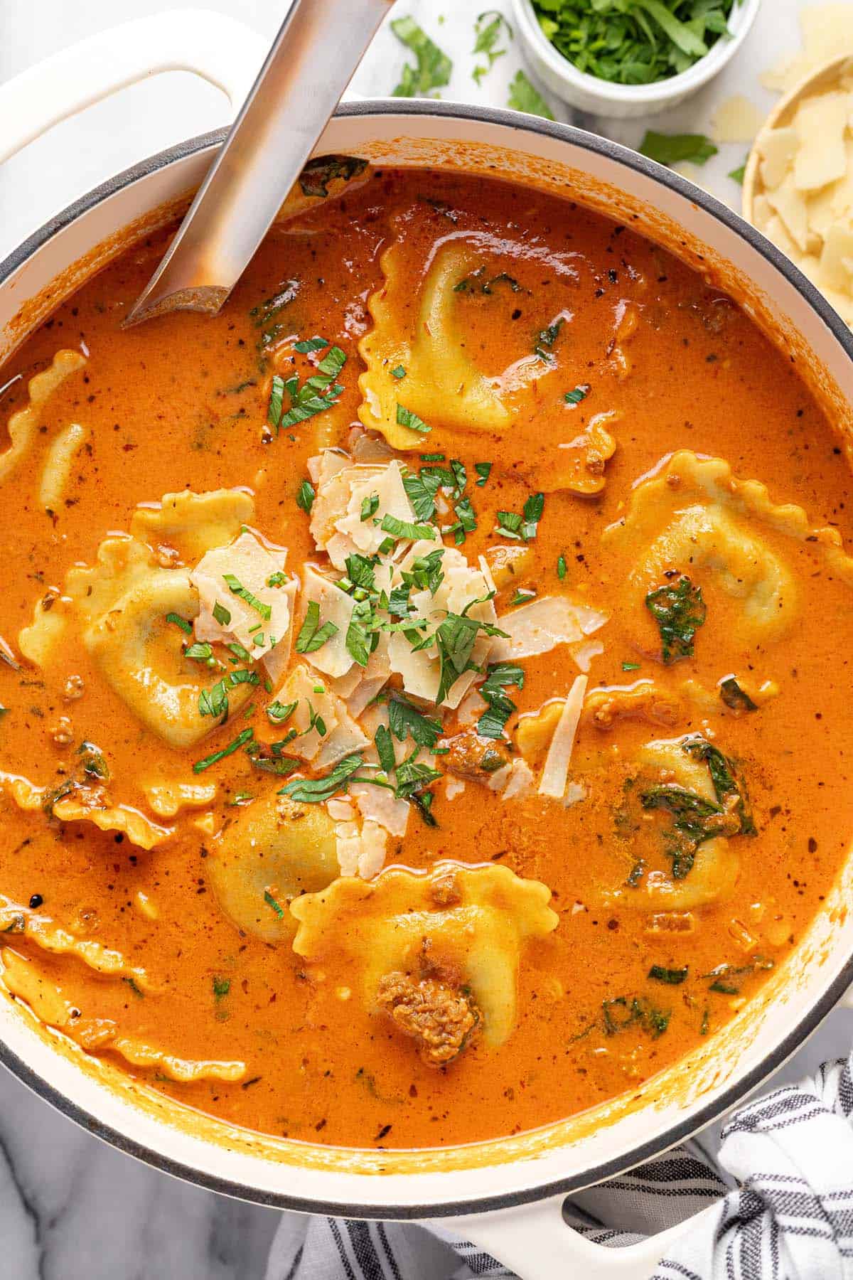 Homeade ravioli soup garnished with Parmesan and parsley in a large pot. 