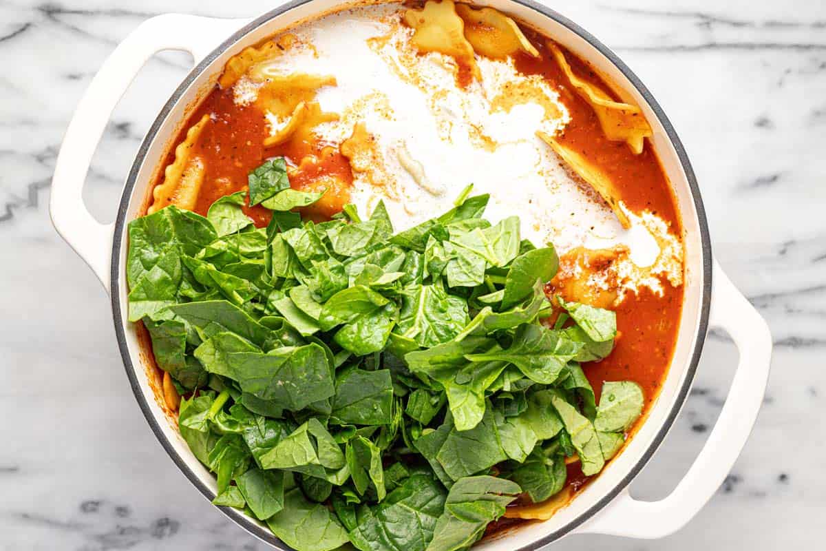 Heavy cream and spinach added to a pot of ravioli soup. 