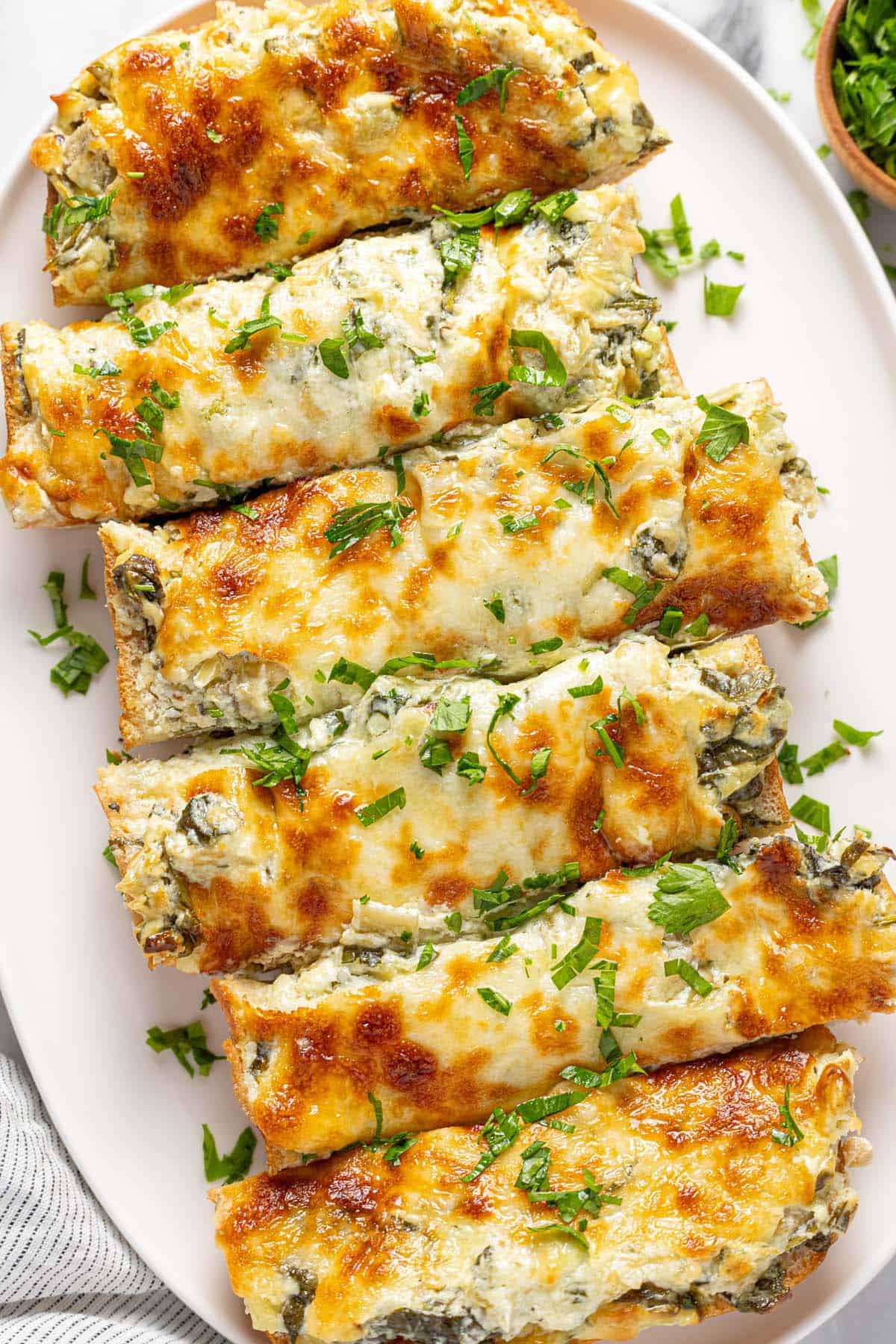 Oval serving platter with sliced spinach and artichoke cheese bread on it. 