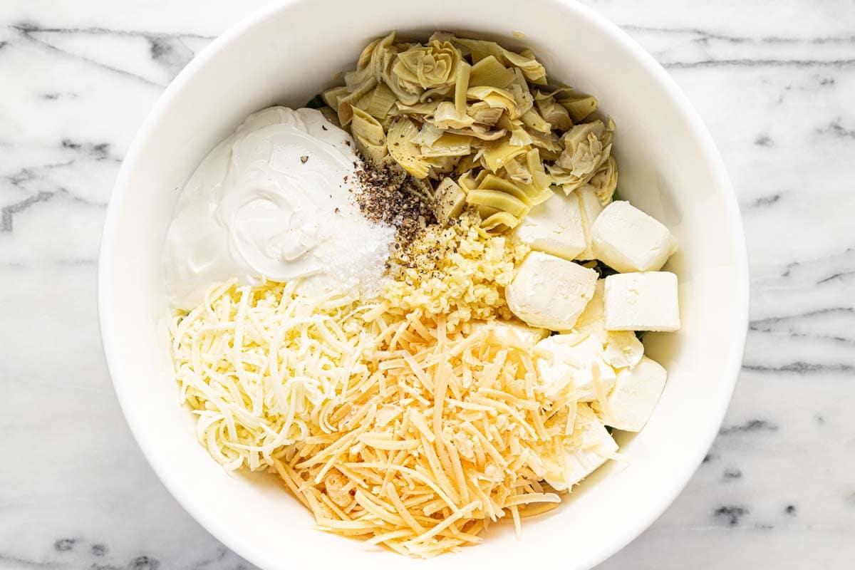 Ingredients for spinach and artichoke dip in a large bowl. 