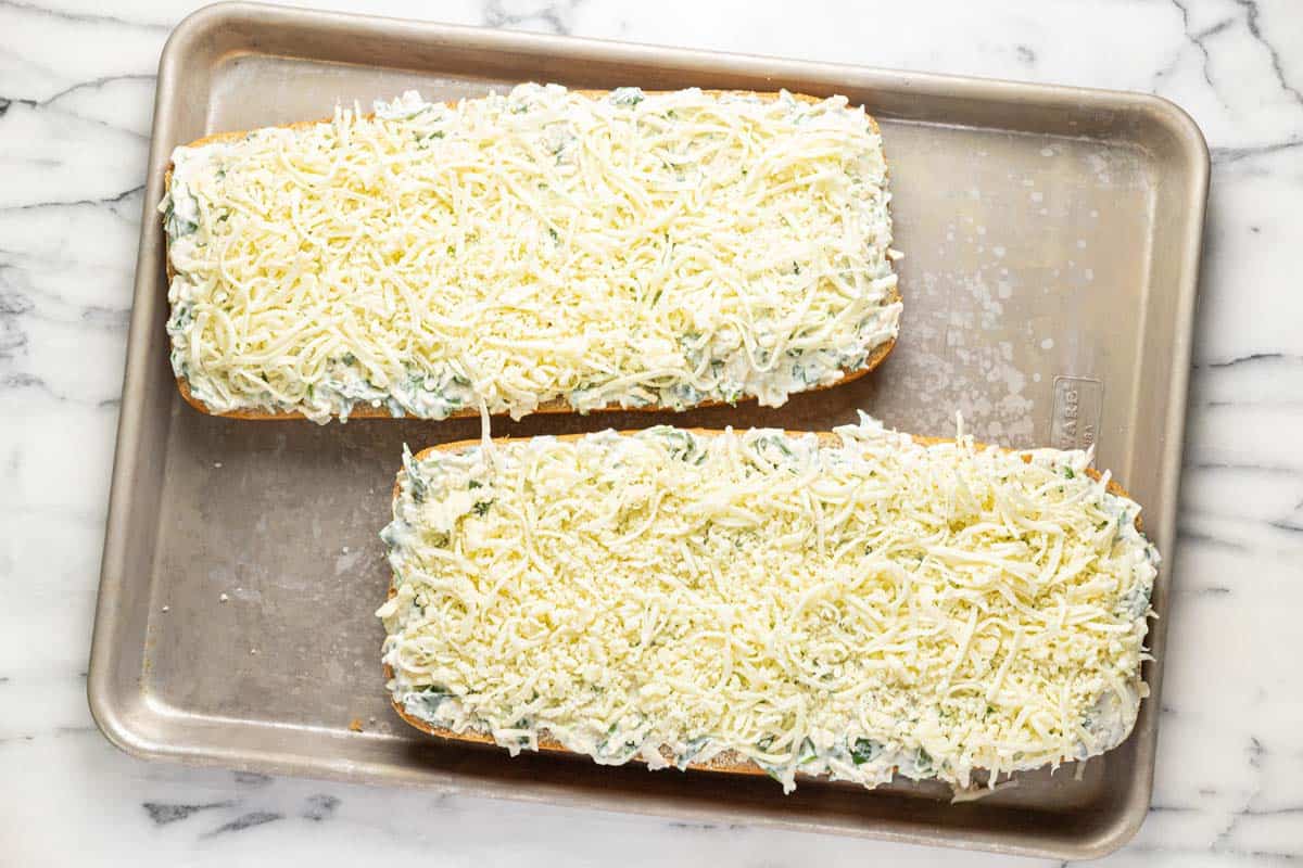 Baking sheet with spinach and artichoke bread topped with shredded cheese. 