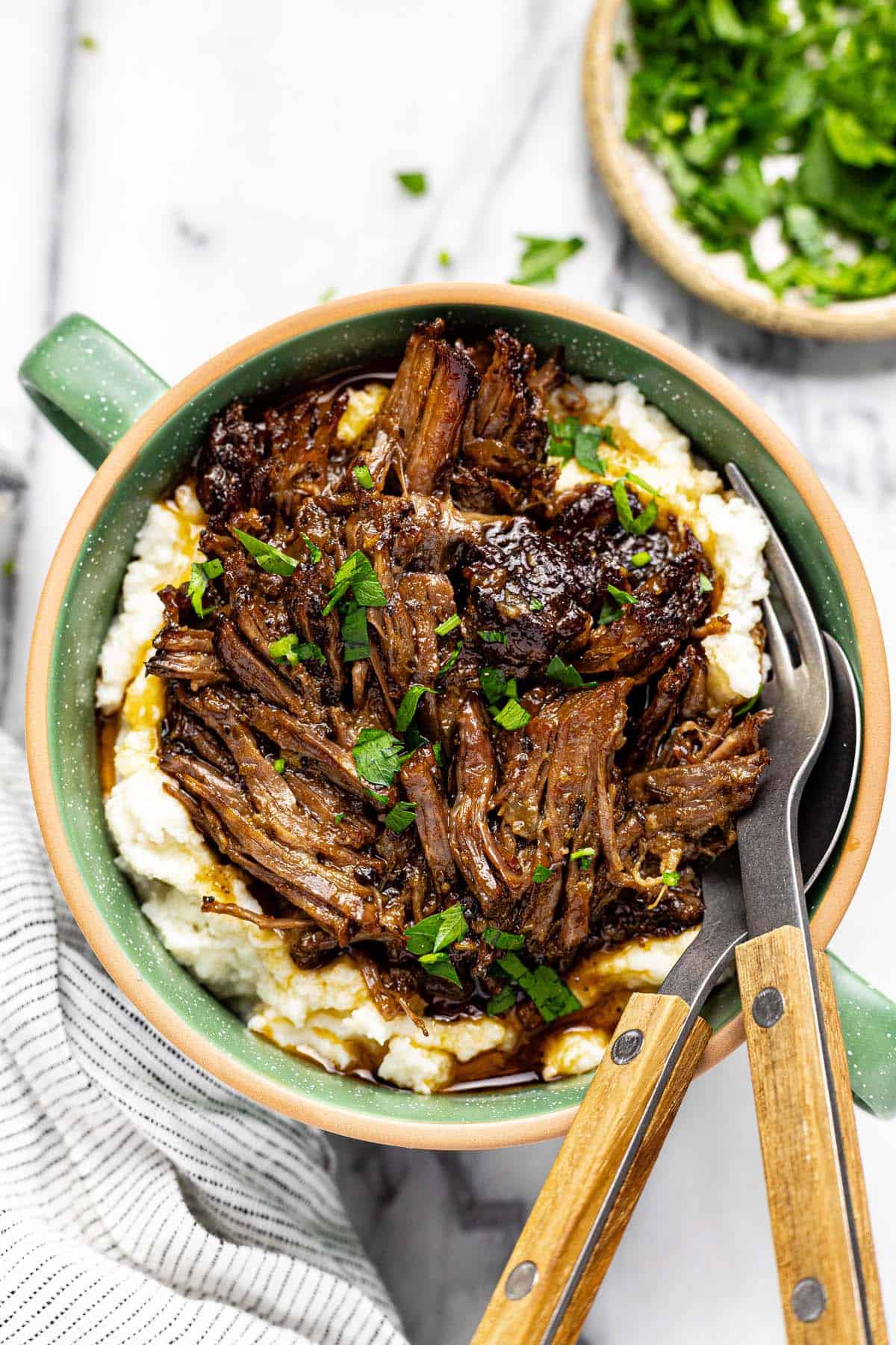 Bowl of mashed potatoes topped with shredded beef chuck roast and parsley. 