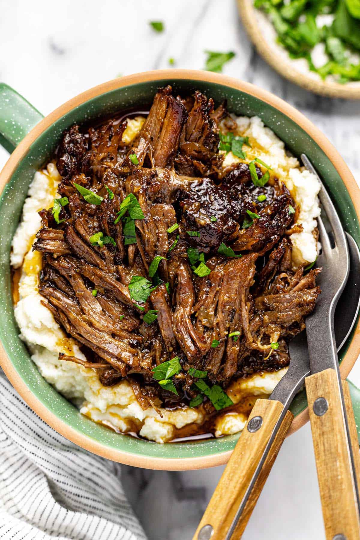 Bowl of mashed potatoes topped with shredded beef chuck roast and parsley. 