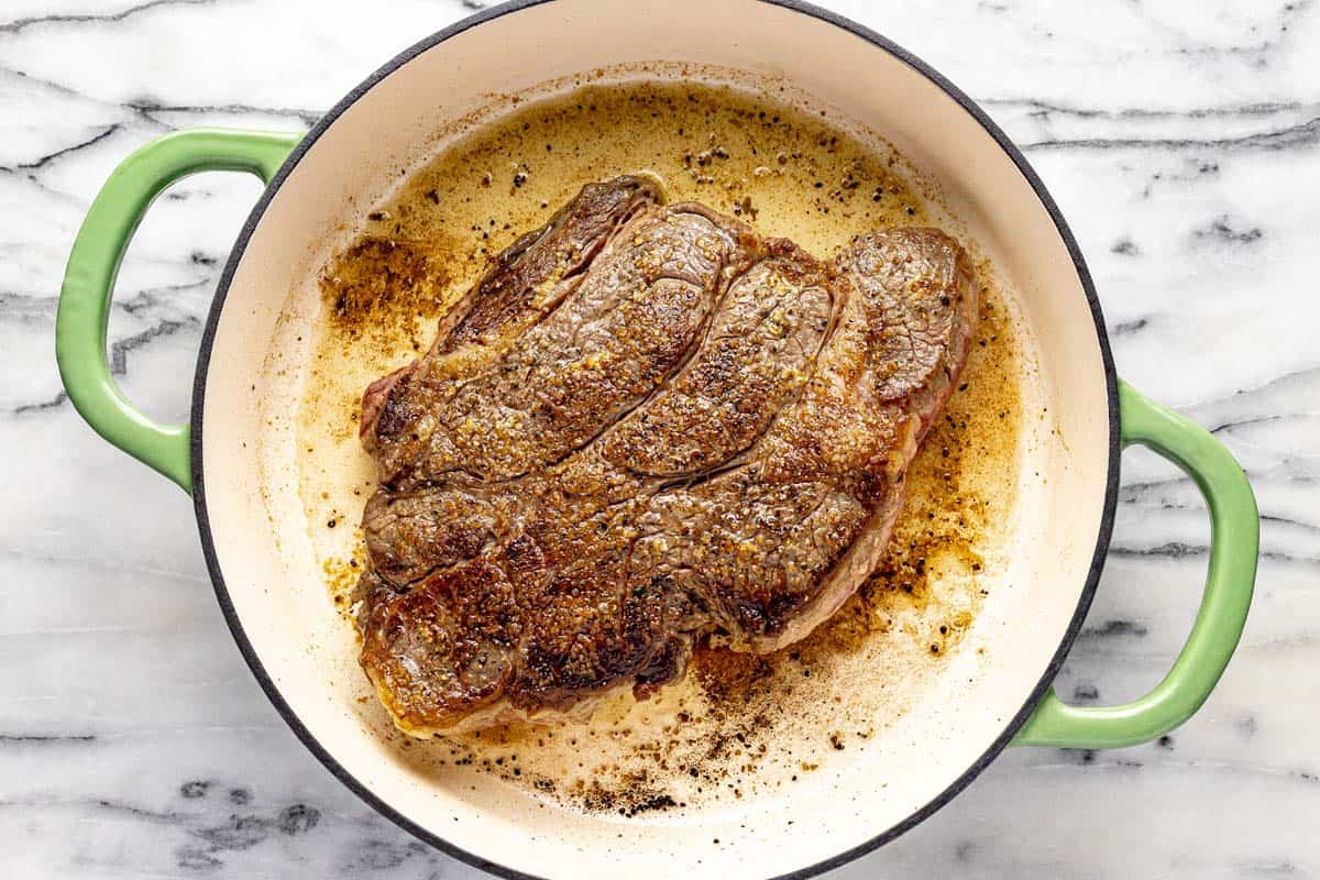 Large braising pan filled with seared beef chuck roast. 