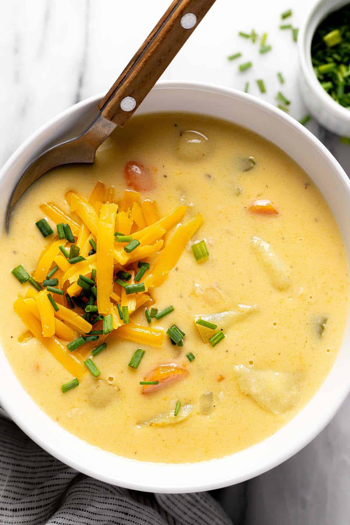 Bowl of cheesy potato soup topped with shredded cheese and chives. 