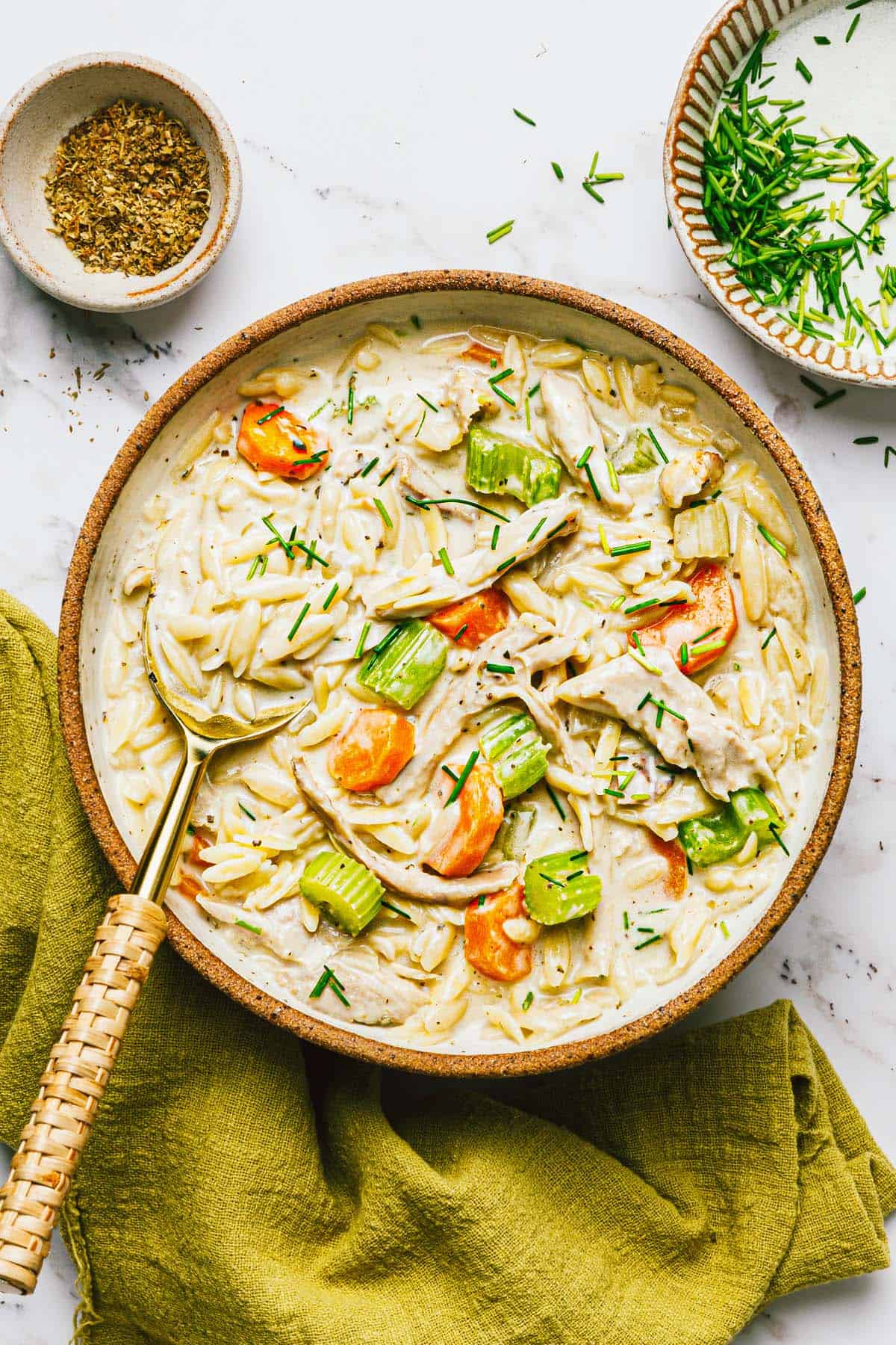 Bowl of creamy chicken and orzo pasta garnished with chives. 