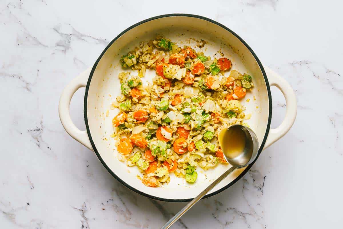 Large pot of sauteed veggies coated in flour with a ladle adding broth. 