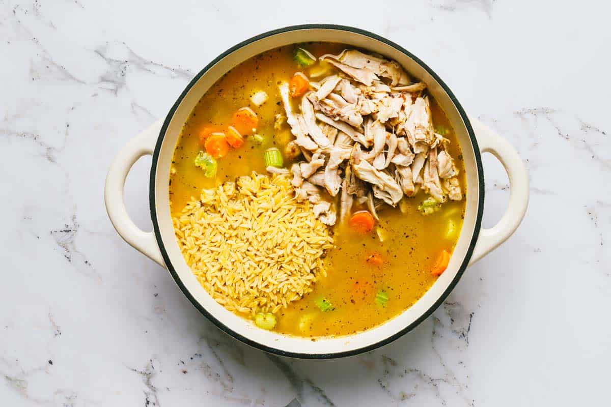 Large pot filled with ingredients to make creamy chicken orzo soup. 