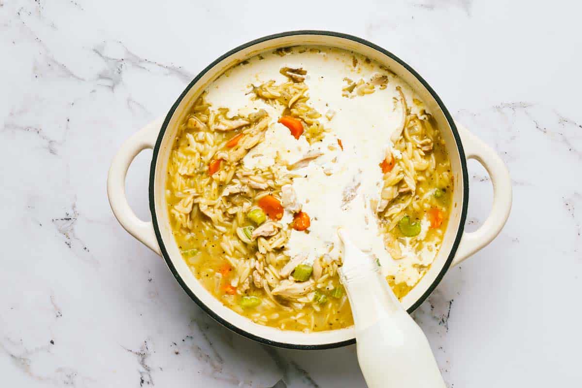 Cream being poured into chicken and orzo soup. 