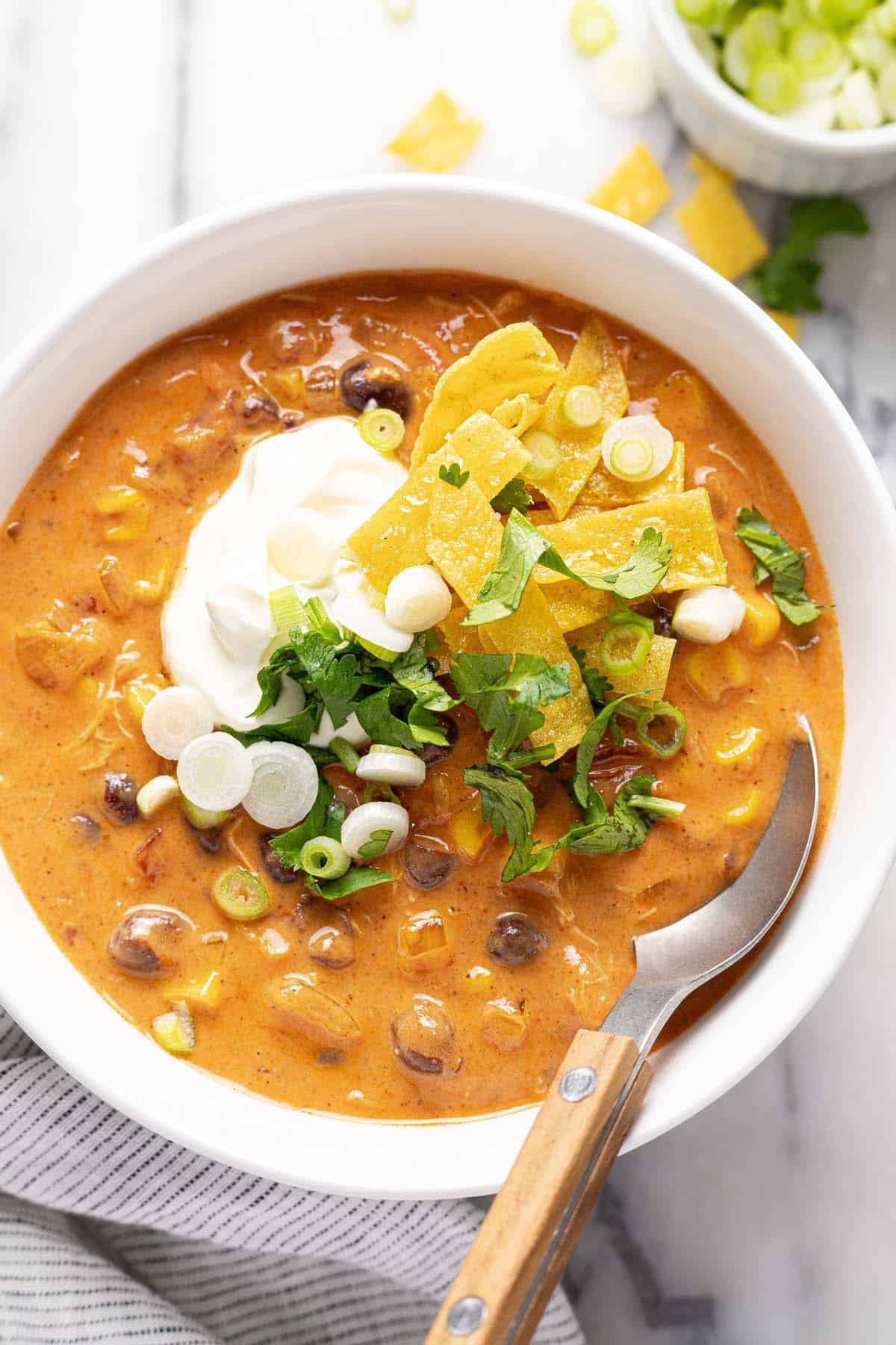 Bowl of creamy chicken tortilla soup topped with sour cream, tortilla chips, cilantro, and green onion. 