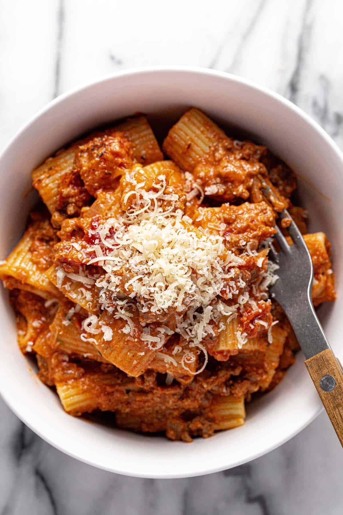 Bowl of ground beef pasta garnished with Parmesan and parsley. 