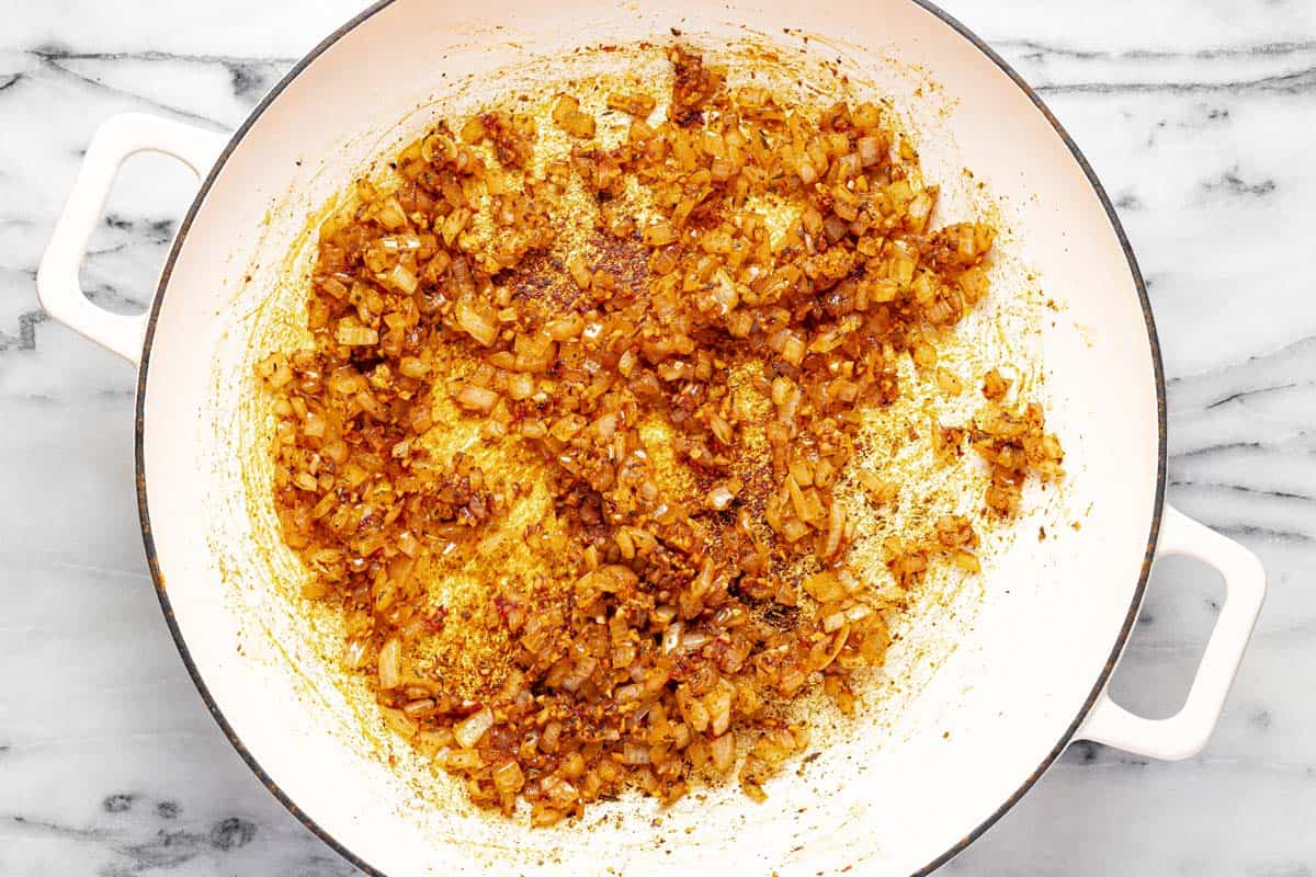 Large pan filled with sauteed onion, garlic, and tomato paste. 