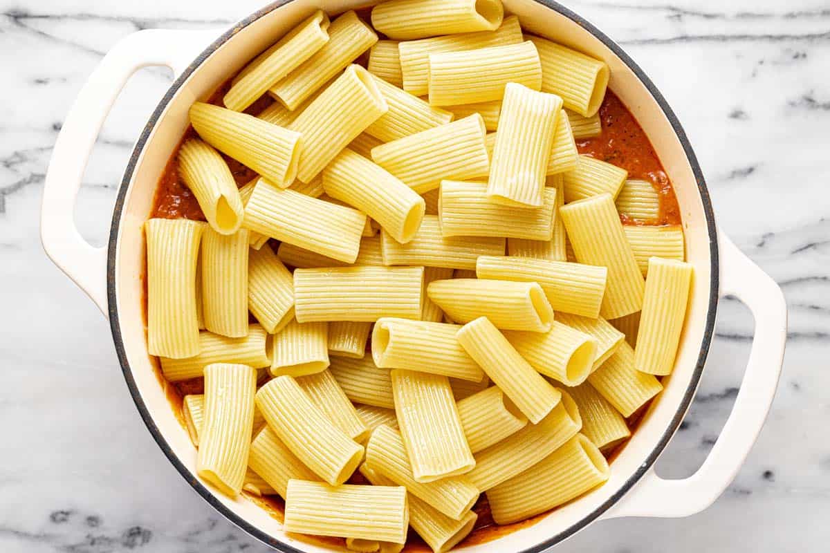 Cooked pasta added to a large pot of meat sauce. 