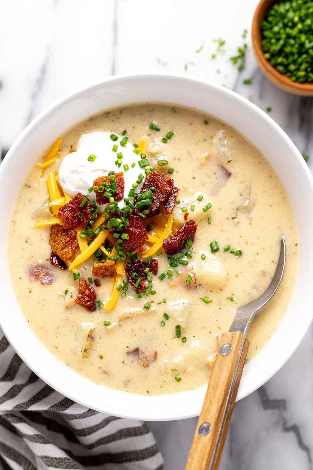 Bowl of loaded baked potato soup topped with sour cream, bacon, and shredded cheese. 