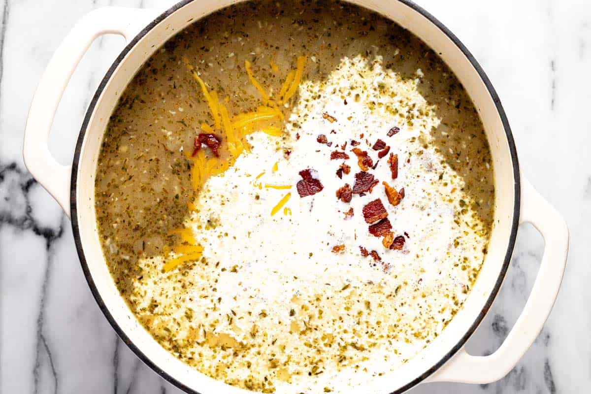 Heavy cream, bacon, and shredded cheese being added to a pot of potato soup. 