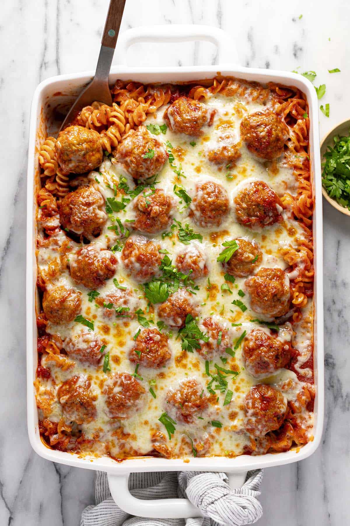 Homemade meatball casserole in a large pan garnished with parsley. 