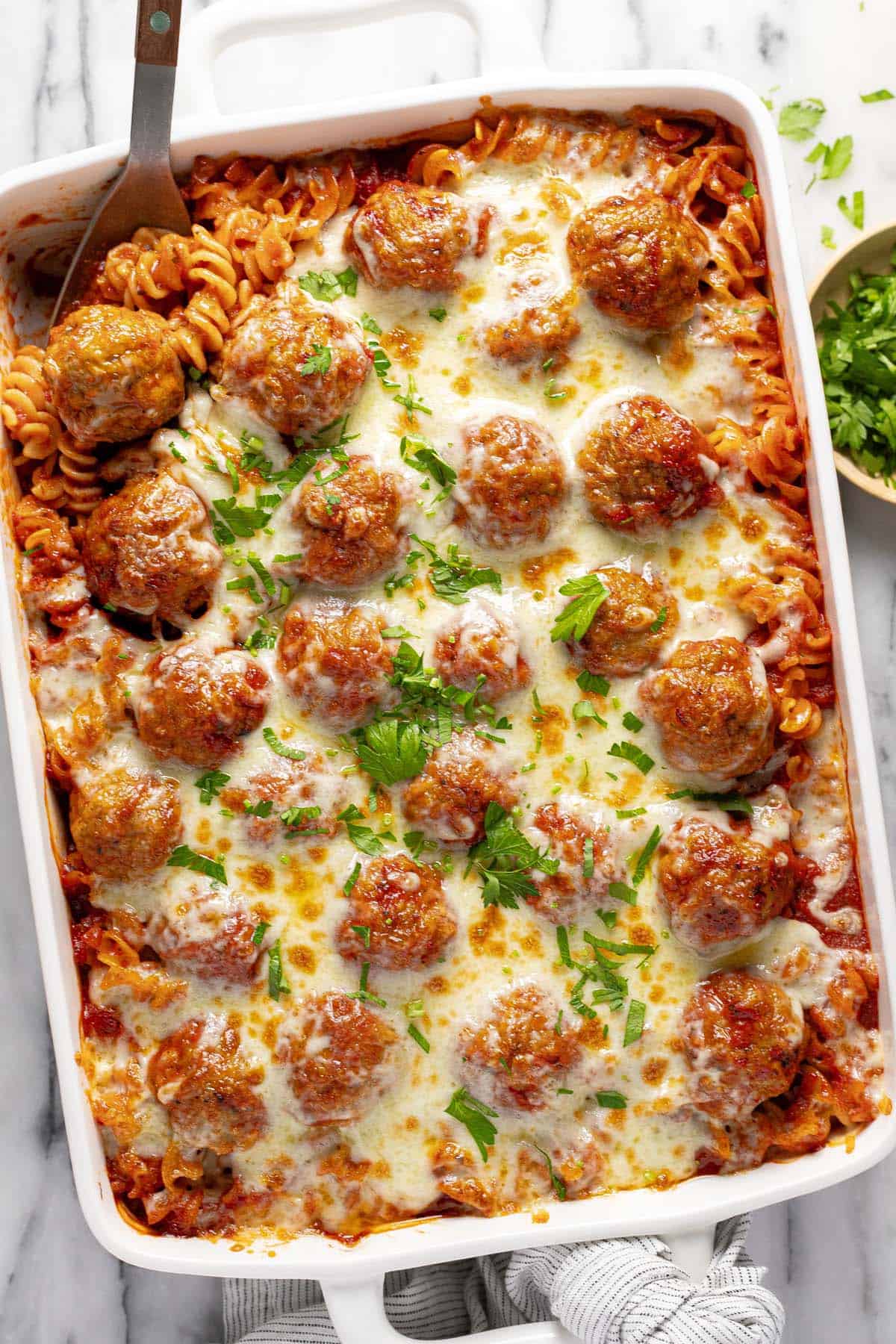 Large pan filled with homemade meatball casserole garnished with parsley. 