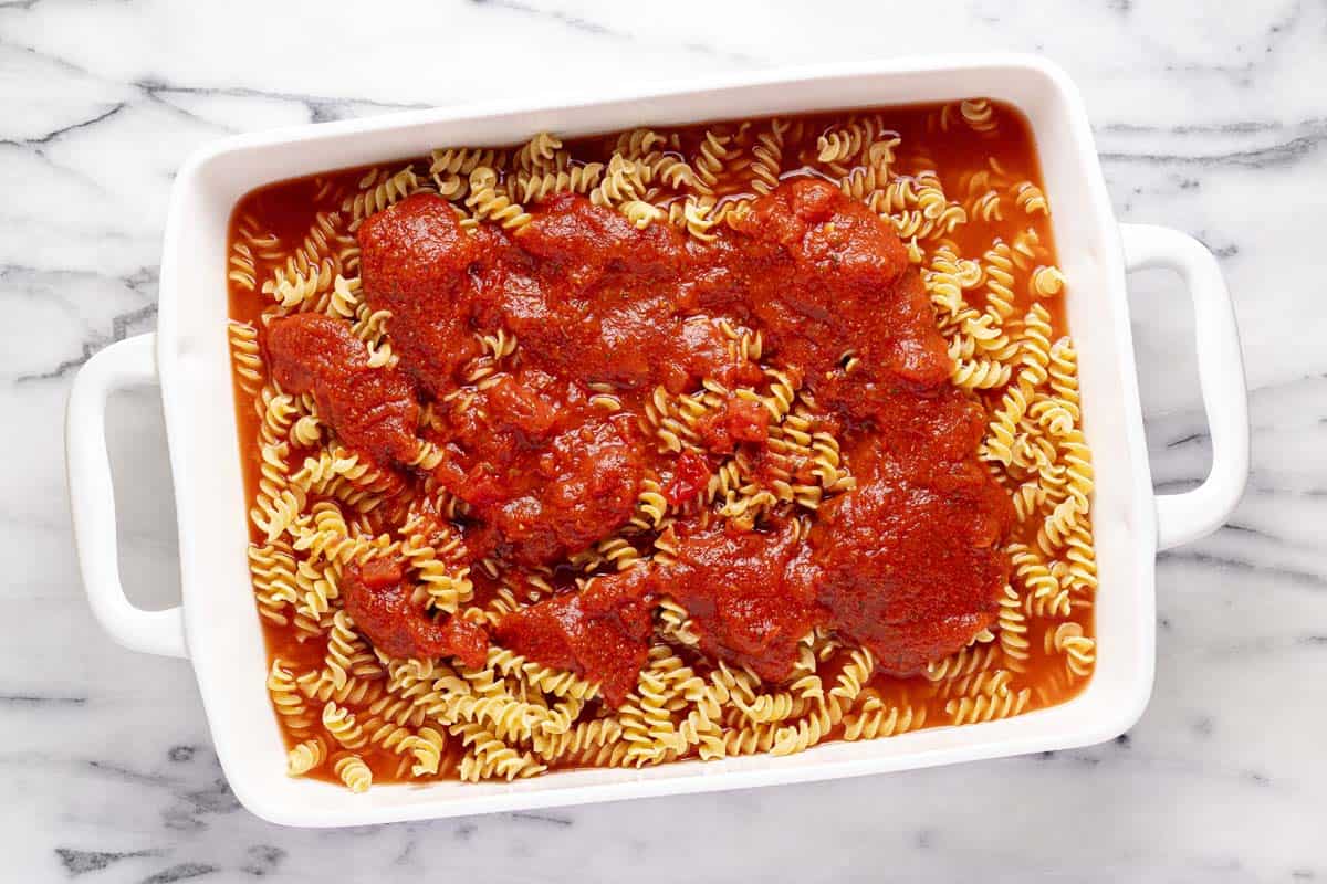 Large pan filled with pasta, spaghetti sauce, and water. 