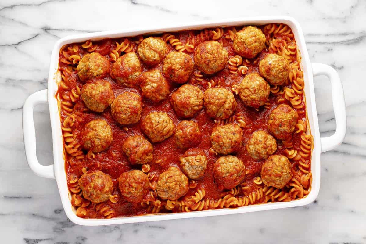 Large pan filled with cooked noodles and meatballs in spaghetti sauce. 