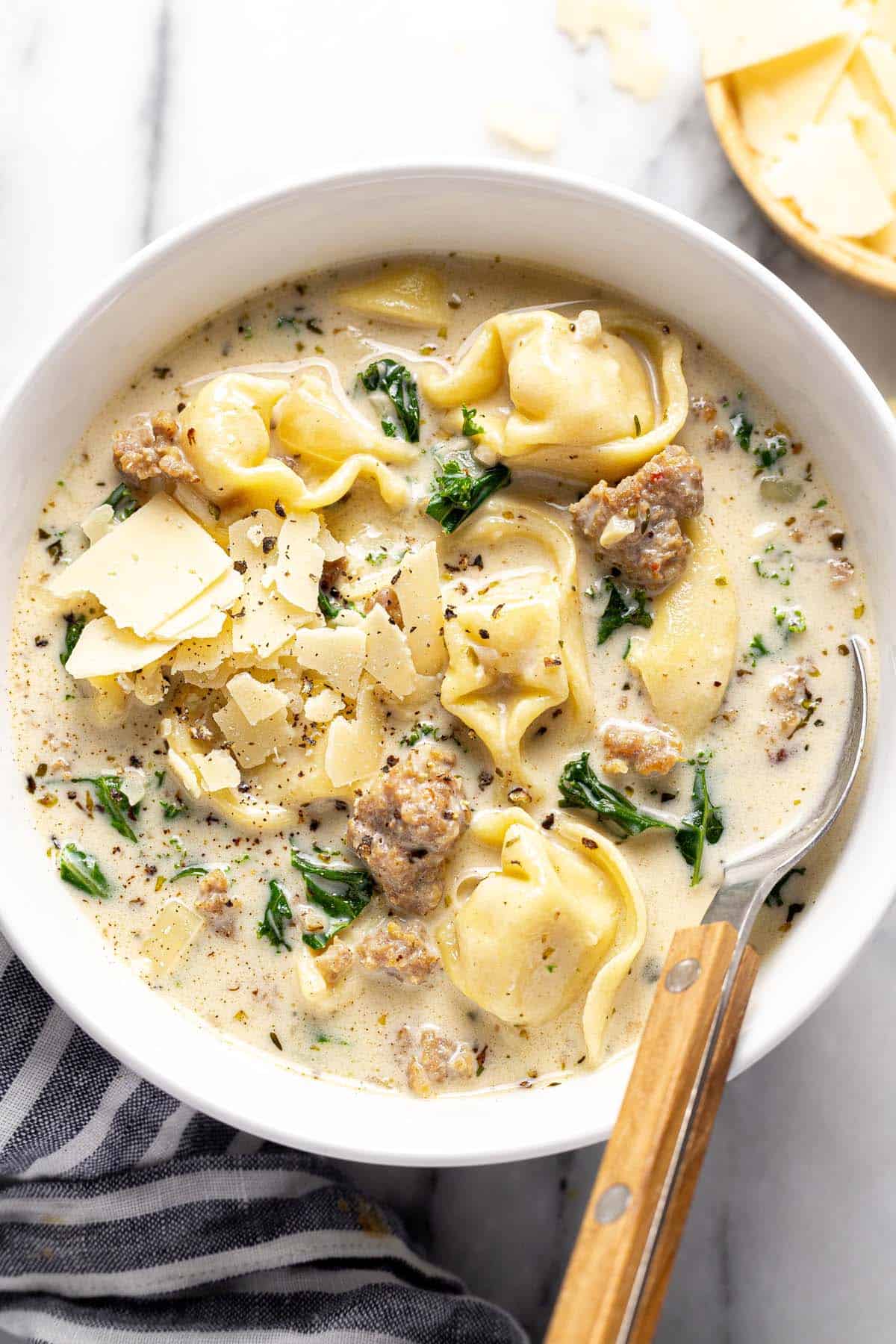 Bowl of sausage tortellini soup with kale garnished with shaved Parmesan. 