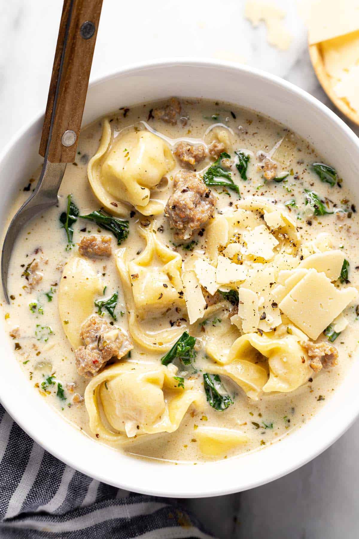 Bowl of sausage tortellini soup with kale garnished with shaved Parmesan. 