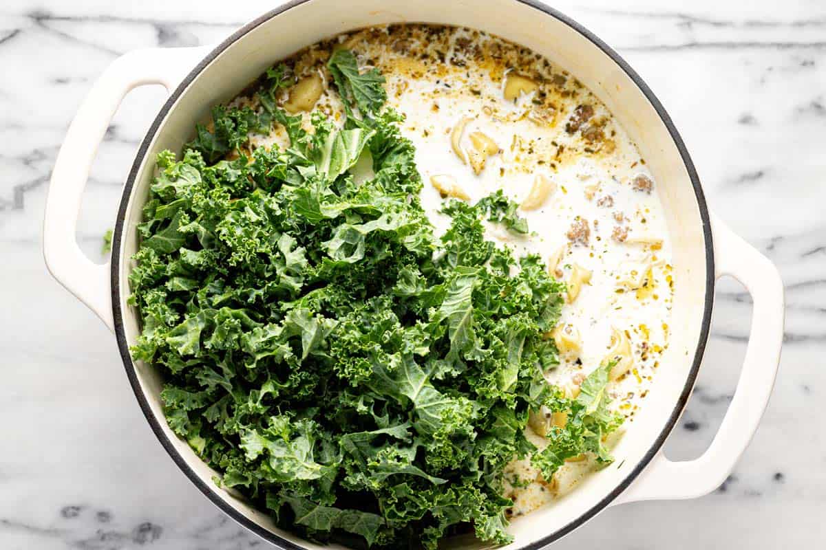 Heavy cream and kale being added to a large pot of soup. 