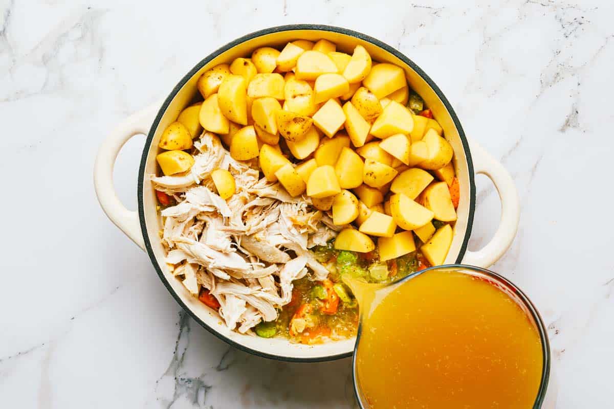 Potatoes, chicken, and veggies in a pot with stock being poured in. 