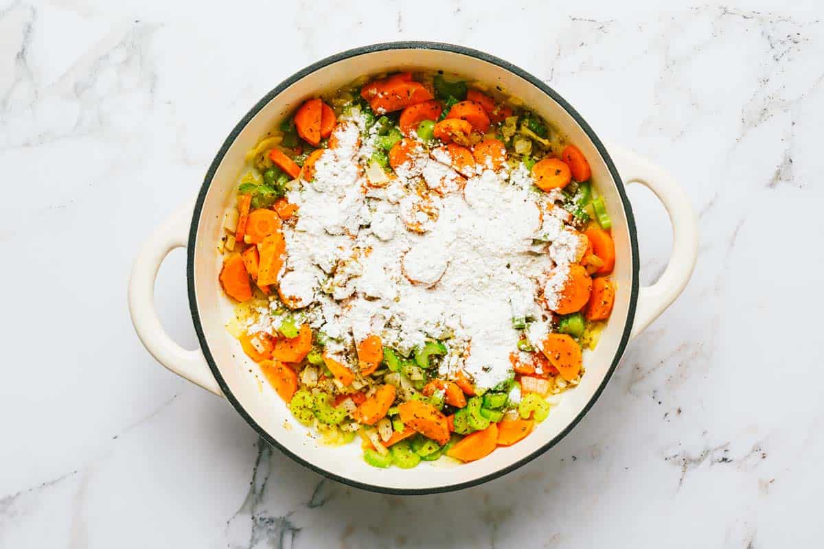 Large pot with sauteed veggies and flour sprinkled on top. 