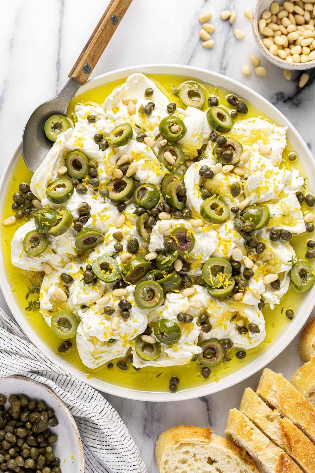 Large serving plate with burrata cheese, garlic olive oil, olives, and pine nuts. 