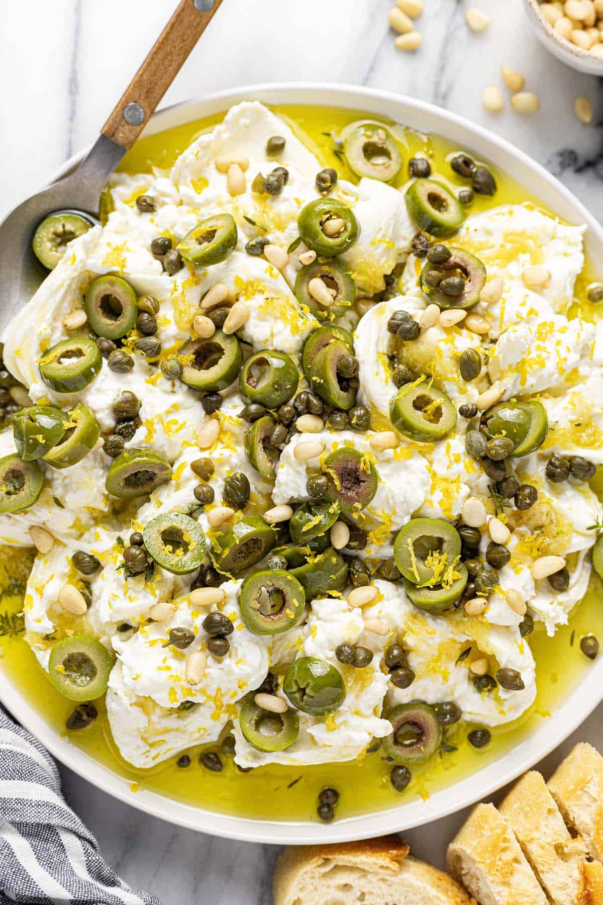 Large serving plate with burrata cheese, garlic olive oil, olives, and pine nuts. 